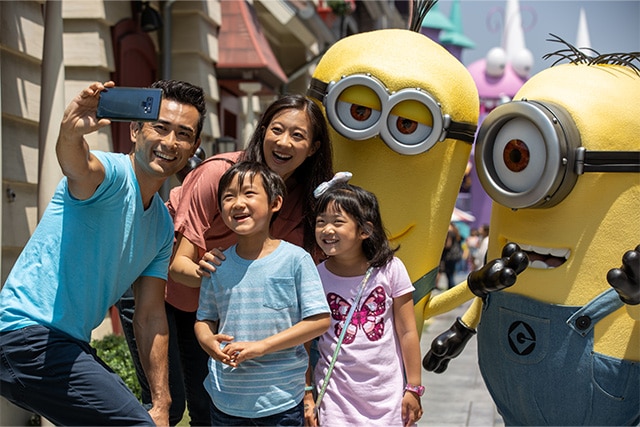 A smiling family takes a selfie in front of two Despicable Me Minions.